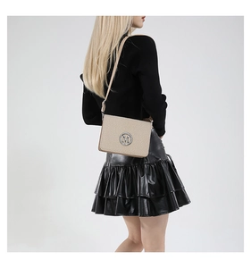 Detail of beige woven texture crossbody camera bag with silver metal M logo on model