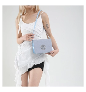 Close-up of a light blue textured camera bag with a silver M logo on a model
