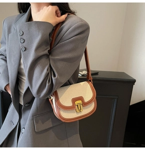 Detail of canvas saddle bag with brown leather trim and golden metal clasp on model