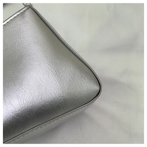 Détail d'un sac baguette argenté montrant le cuir plissé et les coutures soignées