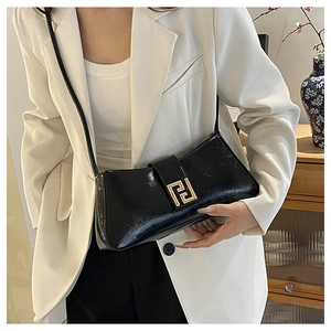 Détail du sac baguette en cuir verni noir avec fermoir doré sur l'épaule du modèle
