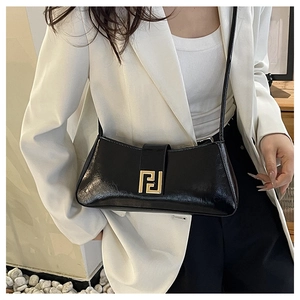 Détail du sac baguette noir brillant avec boucle dorée sur une veste de costume blanche