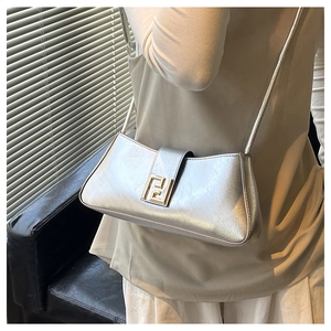 Détail d'un sac baguette argenté brillant avec logo doré et bandoulière en cuir