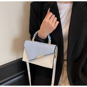 Detail of color-block handbag featuring a blue woven handle and gold metal hardware clasp