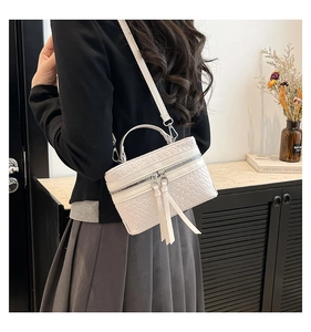 Detail of white woven bucket bag with dual silver zippers and long leather tassels