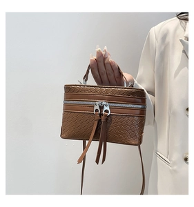 Detailed view of dark brown woven texture handbag with silver zippers and long tassels