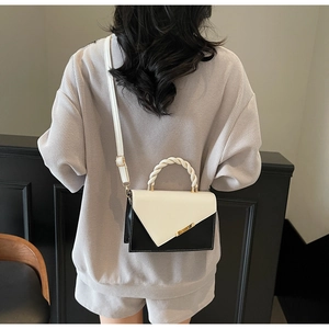 Detail of contrast color crossbody bag featuring white V-flap and woven rope handle