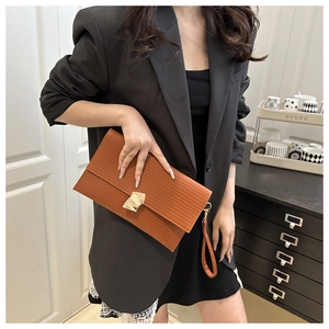 Detail of brown textured envelope clutch bag with gold buckle and wrist strap