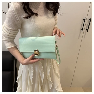Detail of mint green envelope clutch with textured finish and golden geometric lock