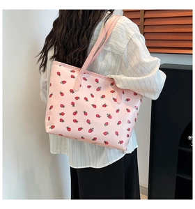 Detail of pink strawberry print tote bag shown on shoulder in a minimalist indoor setting