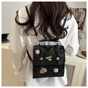 Close-up of black patent leather backpack featuring yellow embroidery and decorative patches