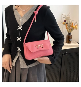 Detail of pink shoulder bag with gold bow clasp and knotted strap on model