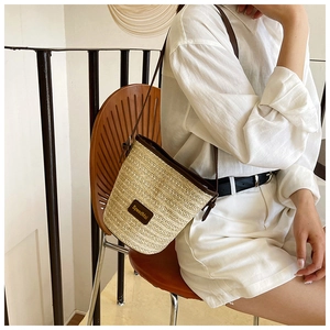 Detail of woven straw bucket bag with dark brown leather straps and branded tag