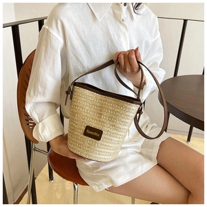 Detail view of woven straw bucket bag with dark brown leather trim and slim strap