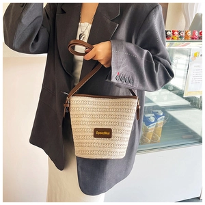 Detail of woven straw bucket bag showing fine beige texture and brown leather strap