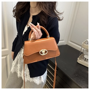 Brown leather crossbody bag with gold lock buckle and top handle shown on a model