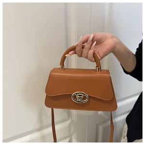 Detail view of smooth caramel leather handbag with gold oval clasp and top handle