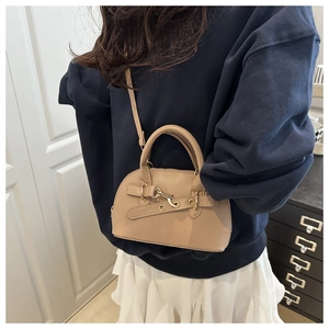 Detailed view of khaki shell bag with gold eyelets worn cross-body with casual outfit