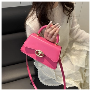 Detail view of pink leather crossbody bag with oval gold lock and elegant top handle