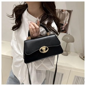 Close-up of a minimalist black leather handbag with a circular gold lock on a white shirt