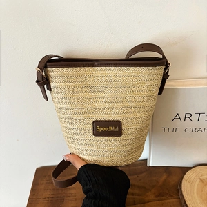Woven straw bucket bag with dark brown leather trim and shoulder strap on wooden table