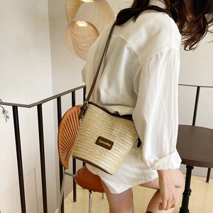 Minimalist woven straw bucket bag with dark brown leather trim and shoulder strap