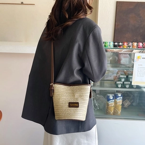 Minimalist beige woven straw bucket bag with brown leather strap for summer vacation