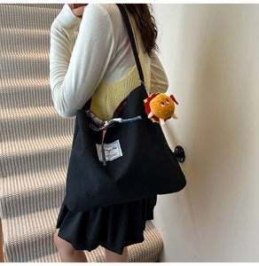 Close-up of black canvas tote bag featuring decorative ribbon and a plush burger charm