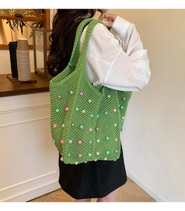 Detail of green knit tote bag with colorful pearl accents and hollow crochet pattern