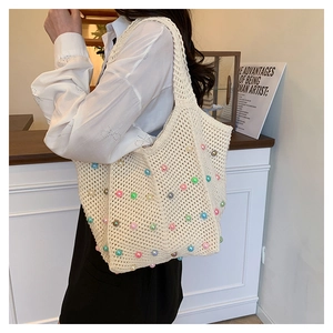 Detail of hand-woven beige tote bag with colorful pearls shown on model's shoulder