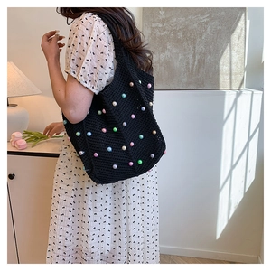 Detail of hand-woven black tote bag with colorful pearl accents on a female model