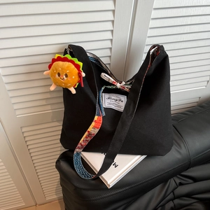 Large black canvas tote bag with geometric strap and burger plush charm on a book