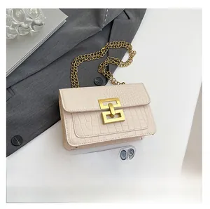 Detalle del bolso crema con diseño de cocodrilo y cadena dorada sobre fondo de traje gris