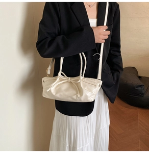 Detail view of a cream dumpling bag with bow decoration and detachable strap