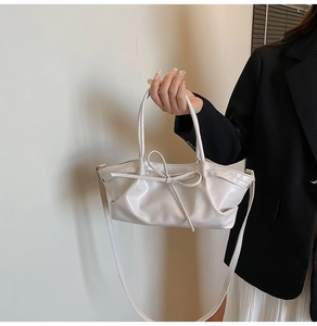 Detail of cream pleated tote bag with bow accent and smooth faux leather texture