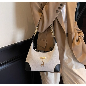 Detail of canvas and leather shoulder bag with golden deer pendant and chain strap