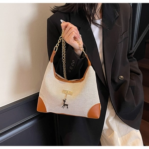 Detail of canvas tote bag with brown leather trim, gold chain, and deer charm