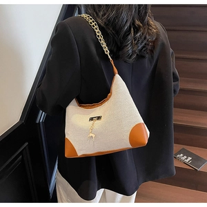 Detail of off-white canvas underarm bag with gold chain strap and deer pendant on model