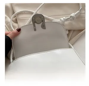Detail of silver magnetic buckle closure on a minimalist white leather saddle bag