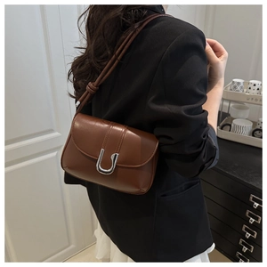 Detail of a dark brown shoulder bag featuring a silver U-shaped metal buckle and knotted strap