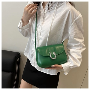 Detailed view of green leather crossbody bag with silver U-buckle on a female model