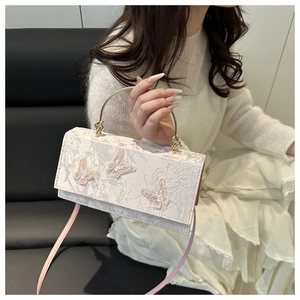 Detail of elegant butterfly embroidery and lace texture on a cream crossbody handbag