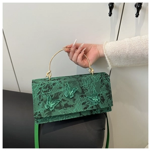 Detail of green lace bag with butterfly embroidery and golden circular metal handle