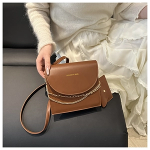Detail einer braunen Lederschultertasche mit Goldkette und passendem Mini-Taschenanhänger
