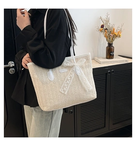 Detail of woven straw bucket bag with delicate white lace bow and shoulder strap