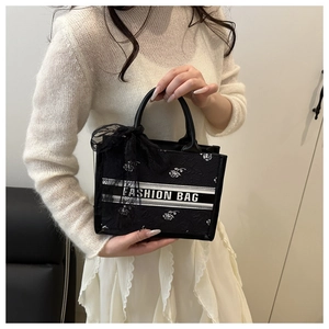 Detail of black tote bag with white rose embroidery and lace bow on handle