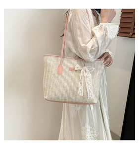 Detail of handwoven straw tote bag featuring pink leather trim and white lace bow