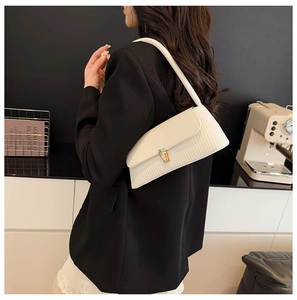 Detail of a beige pleated shoulder bag with a gold twist lock worn over a black blazer