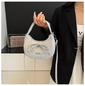 Détail d'un sac à main blanc perle avec nœud tenu par un mannequin en blazer noir