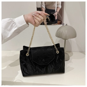 Detail of black pleated texture shoulder bag with elegant gold chain strap and flap closure